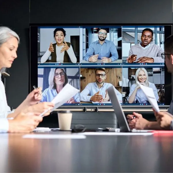 A meeting room screen with a video call of eight people