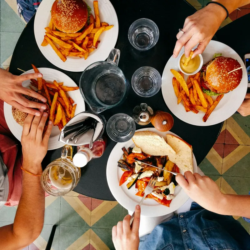 People eating burgers, fries and roasted vegetables at a round table, seen from above